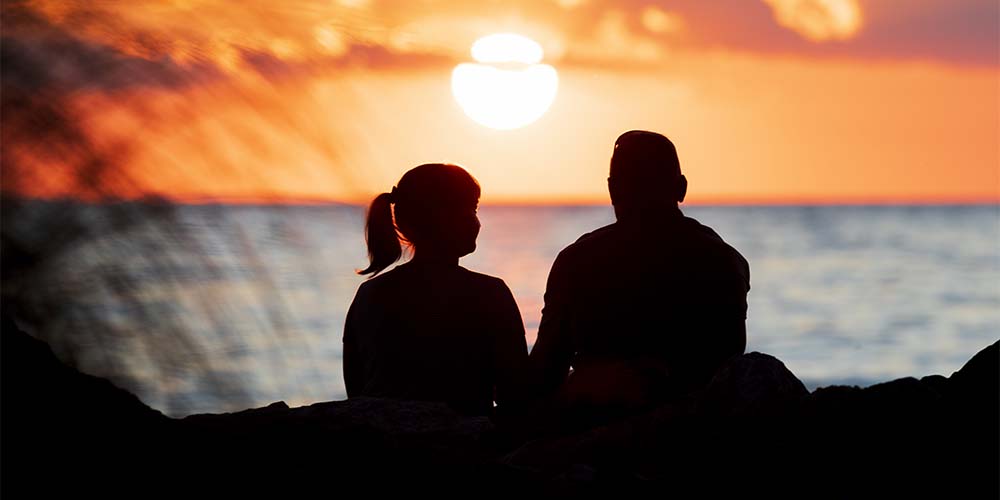A couple sitting on the lake shore enjoying the sunset